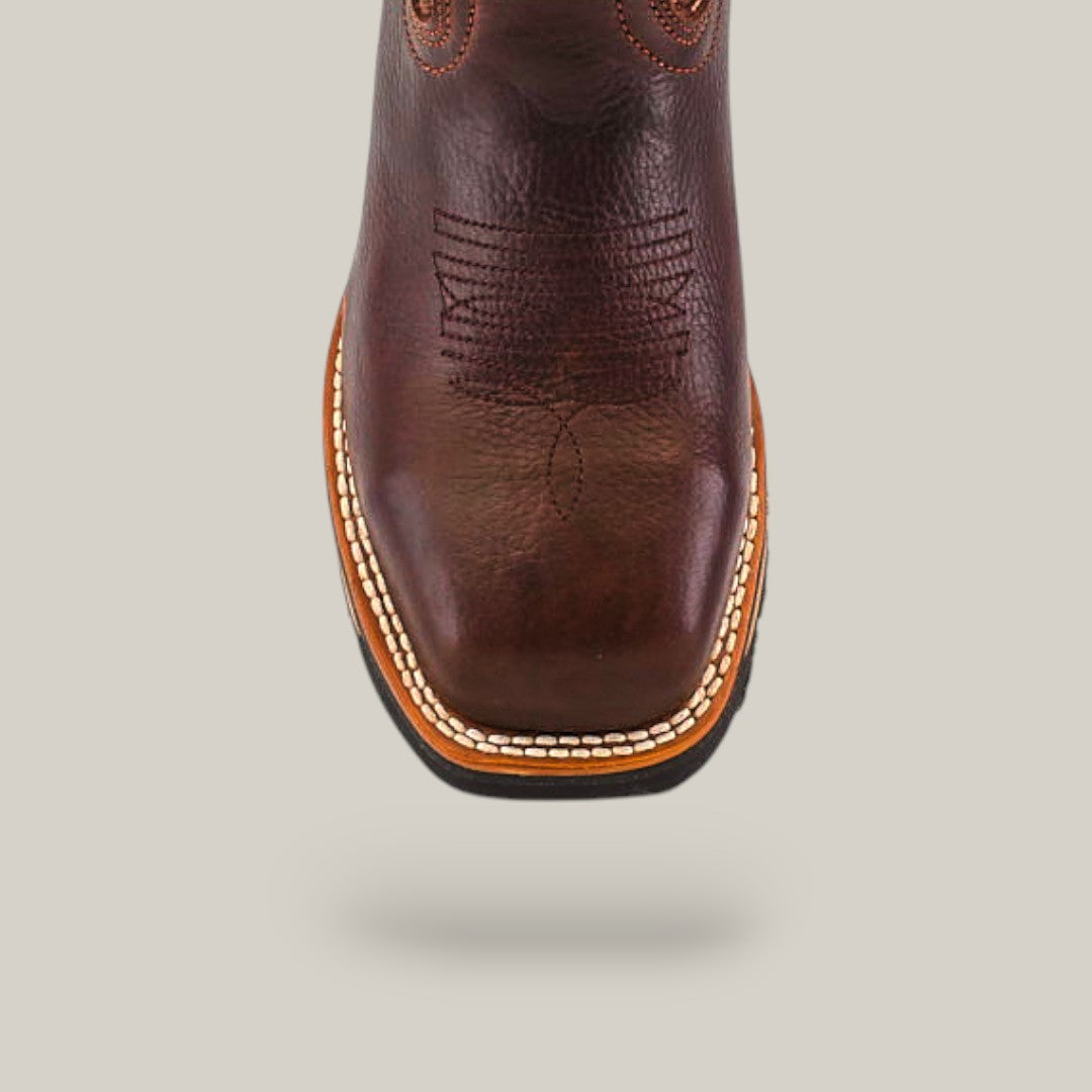 Close-up of the Taurus Moka Composite Toe - E6185, a brown leather boot with decorative stitching and square toe, featuring detailed embroidery, renowned durability, and thick light-colored sole trim against a plain, light background.