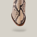 The image features the toe area of the Plunge Natural Python Zipper & Cut Out - Round Toe - CU570 boot in brown and cream snake-print leather. The python design adds texture and style, set against a solid background that highlights the craftsmanship of this unique footwear piece.