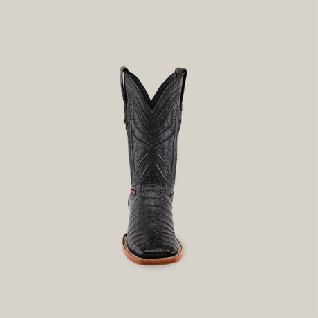 A front view of the Exotic Caiman Belly - Black - Square Toe boot showcases intricate stitching and a textured surface reminiscent of caiman belly, with a refined black design and brown sole against a plain beige background, perfect for true cowboy connoisseurs.