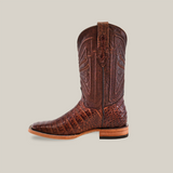 The Exotic Caiman Belly - Brown boot, with intricate stitching and genuine caiman leather, is displayed on a light beige background. It features a square toe and low wooden heel, highlighting its unique craftsmanship.