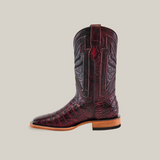 The Exotic Caiman Belly - Black Cherry - Square Toe is a single dark red cowboy boot with intricate patterns and a low heel. It features detailed stitching, a wooden sole, and embodies the craftsmanship of square toe boots against a plain background.