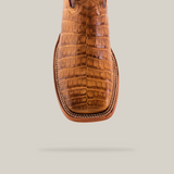 A close-up of the Exotic Caiman Horn Back - Brown - Square Toe boot features its crocodile texture and detailed stitching on genuine leather, centered on a plain, light background.