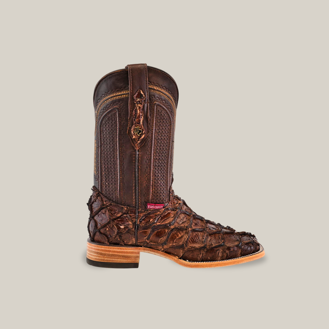 The Exotic Piraruco Fish - Brown - Square Toe cowboy boot is crafted from pirarucu leather with a reptilian texture on the foot. It features a darker, smooth shaft with subtle stitching and rests on a light sole with an elevated heel, ideal for Western wear.