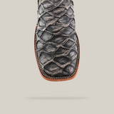 Close-up of the Exotic Piraruco Fish boot, highlighting its textured scaly design and dark leather. The square toe features rustic bone stitching on the edge, set against a light beige background.