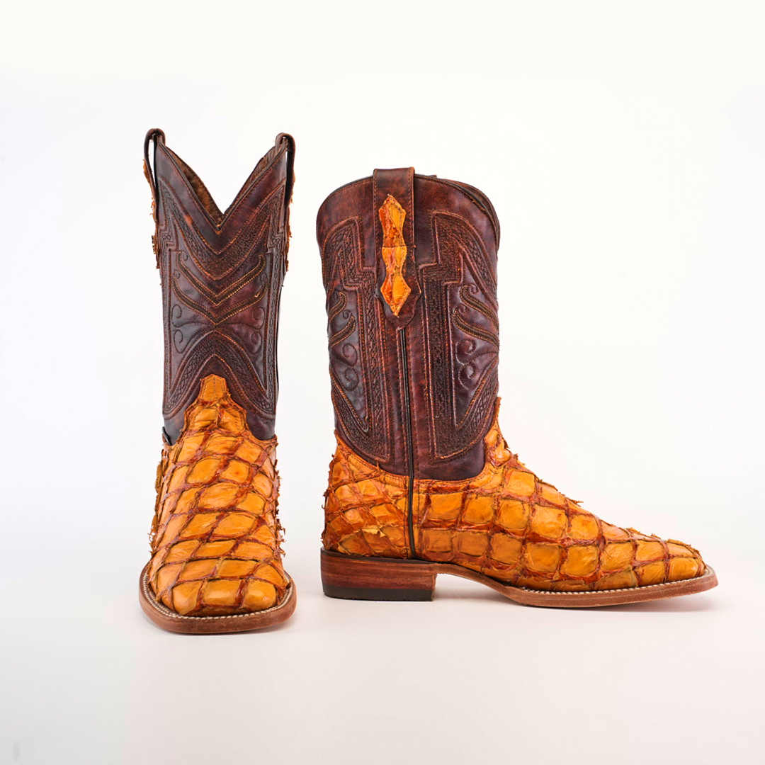 A pair of Exotic Piraruco Fish - Brandy Square Toe cowboy boots with intricate brown leather tops and textured orange fish leather scales on the lower part, standing upright against a white background.