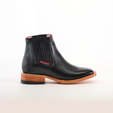 The Napa Black Square Toe boot features black Napa leather with a square toe design, brown wooden sole, slight heel, side elastic panels, and a decorative red tag on plain white background. Perfect addition to the fashion-forward wardrobe.