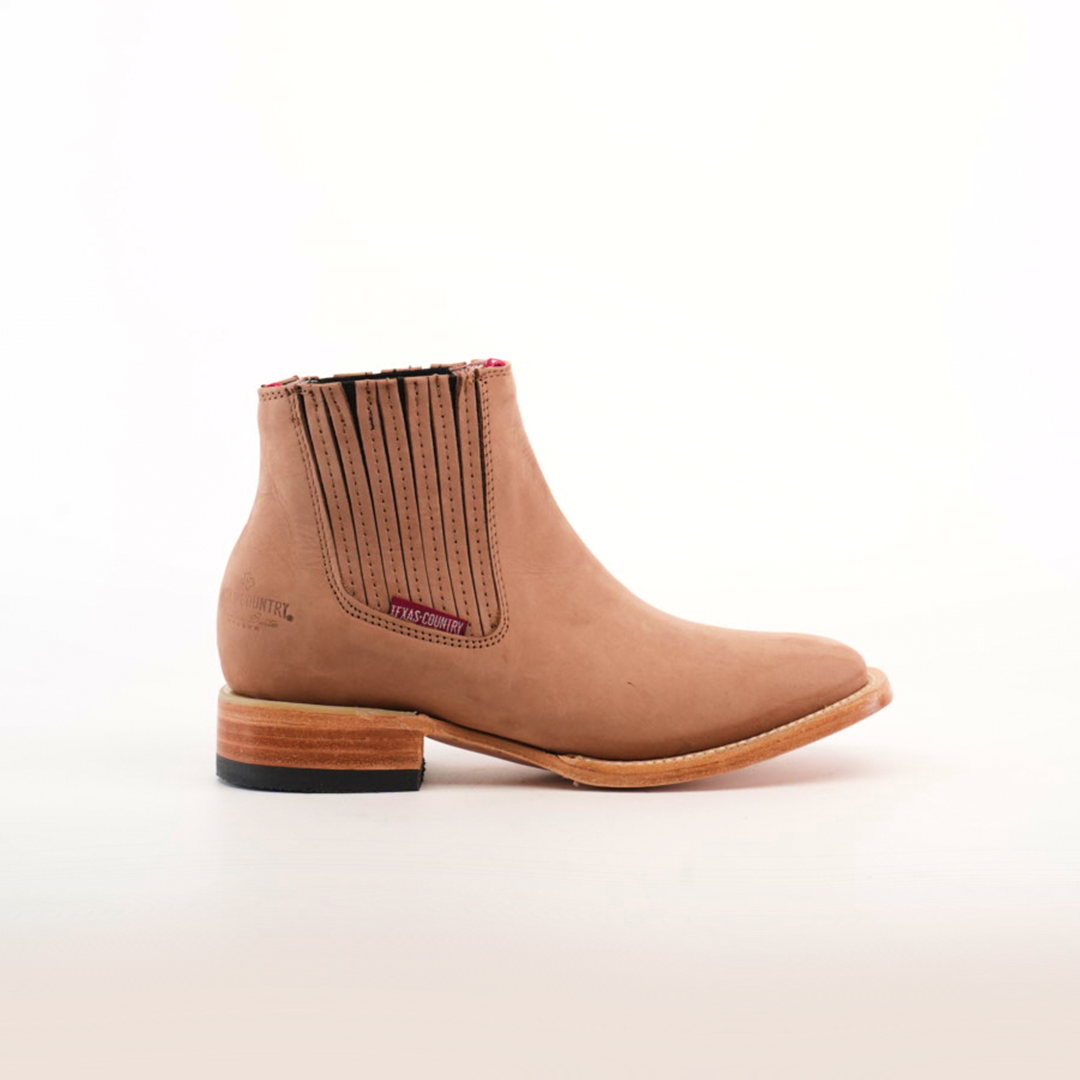 The Prime Suede Sand Square Toe is a tan leather ankle boot with elastic side panels and a pull tag, ideal for a fashion-forward wardrobe. It boasts a low wooden heel with a black sole and has a subtle brand logo embossed near the heel. Displayed against a plain white background.