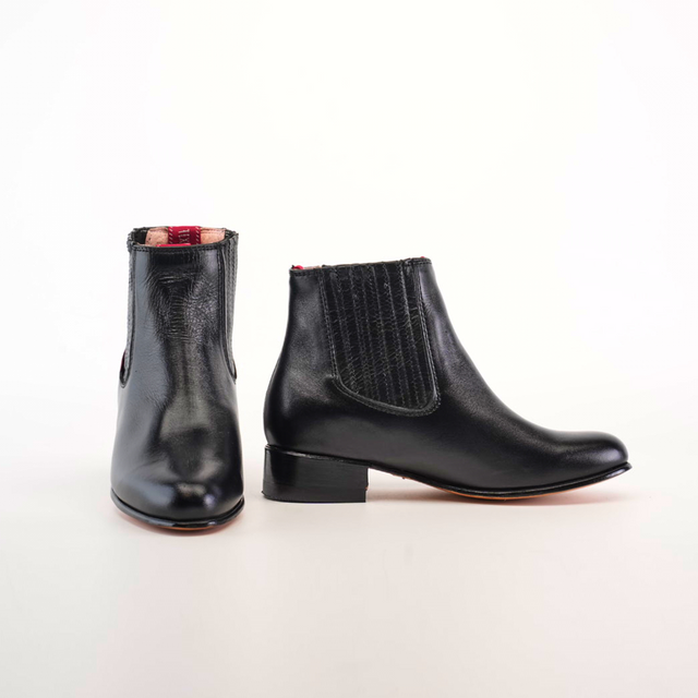 The Napa Black Square Toe Ankle Boots are a sleek addition to any fashion-forward wardrobe. With the left boot showcasing its square toe and the right revealing a textured side panel and red interior lining, these handcrafted boots stand out elegantly against a plain white background.