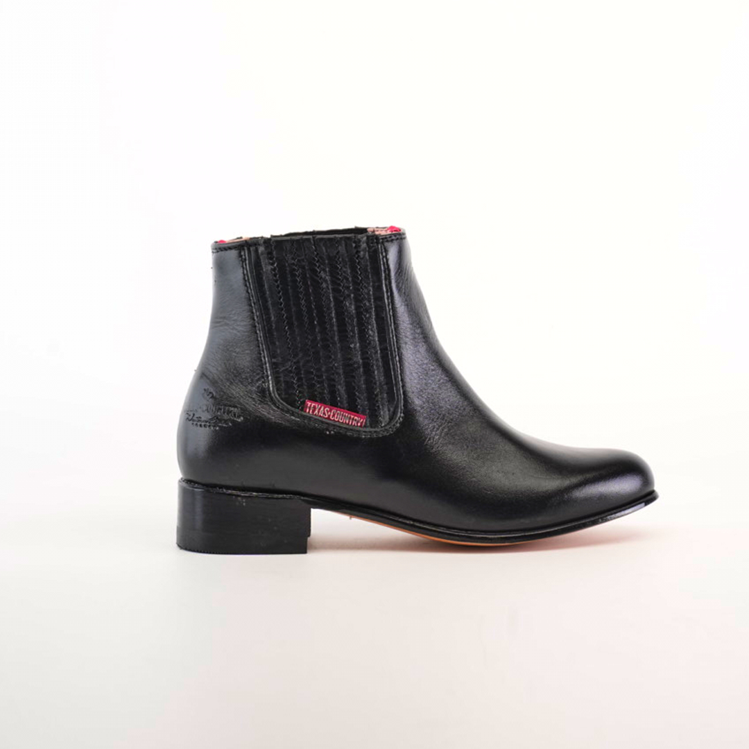 Introducing the Napa Black Square Toe, a modern wardrobe staple. This handcrafted black leather ankle boot showcases elastic side panels, a low heel, and subtle red stitching near the top edge, all set on a plain white background.