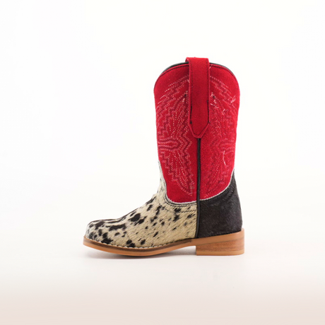 The Cowhide Hair Pinto Square Toe childrens cowboy boot features a western style, with a red shaft adorned with embroidered star patterns and a spotted black and white cowhide hair pinto shoe, complete with a light brown sole. The boot is shown from the side against a white background.