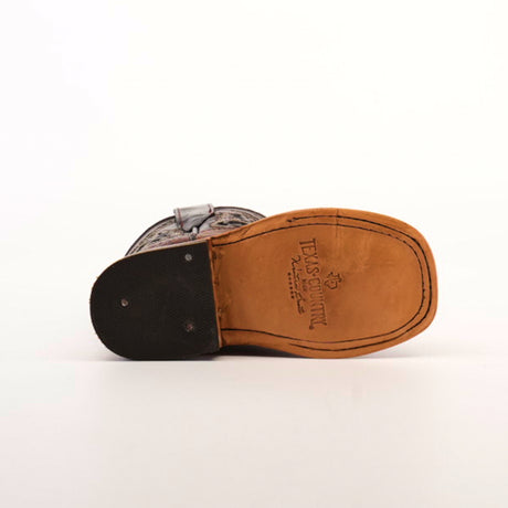 The image features the bottom of a Western-style Caiman Hornback Print Chocolate Square Toe boot with a tan leather sole and black heel. Engraved text and a TEXAS COUNTRY logo adorn the sole, showcasing exquisite craftsmanship against a plain white background.