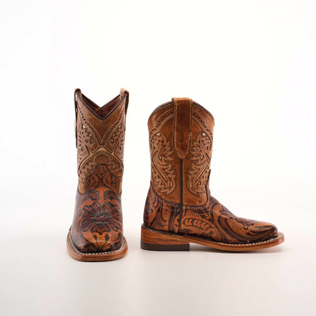 The Handtooled Leave Orix Square Toe cowboy boots, crafted from rich cowhide leather, feature detailed floral patterns. With one boot upright and the other tilted to display the design, these handcrafted boots showcase a thick heel and embody traditional Western craftsmanship.