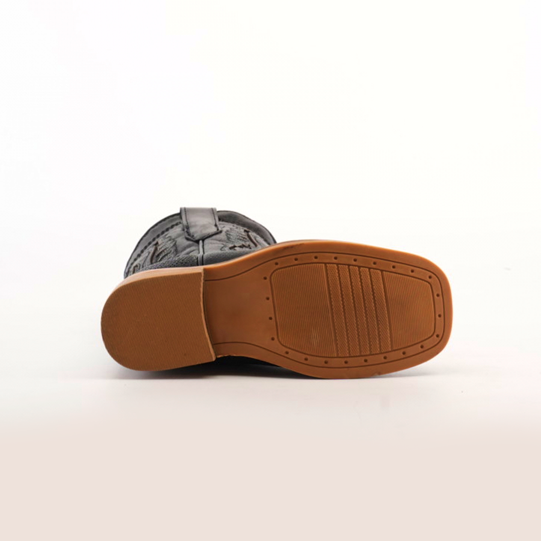 The image displays the bottom view of a Stingray Half Cowhide Print Black Rodeo Toe shoe, featuring a patterned black upper and tan rubber sole. The sole has a rectangular textured area and small circular indentations reminiscent of tiny Stingray boots.