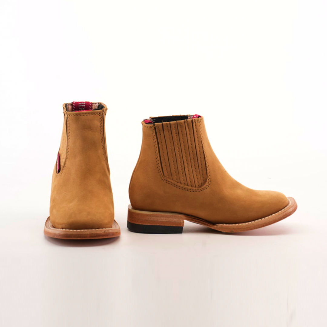 Two Prime Suede Honey Square Toe boots are shown on a white background. The tan leather Chelsea boots have reddish plaid lining, brown soles, and elastic goring; the left boot displays the inner side and the right shows the outer side.