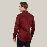 A man in a Men’s Single Pocket Logo Modern Fit Stretch Dress Shirt - Burgundy (CTL9260) and black pants stands with his back to the camera against a plain gray background.