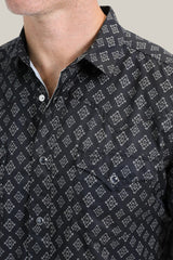 The individual is wearing the Mens Performance Western Short Sleeve Aztec Print Black Shirt (PGW10630) with silver buttons, a chest pocket, a black quick-dry fabric featuring a white Aztec geometric pattern. The image displays them from shoulders to chest against a plain background.