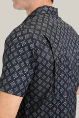 A close-up shows someone in a Mens Performance Western Short Sleeve Aztec Print Black Shirt (PGW10630) with a unique back flap. Their left arm is visible against a light gray background, highlighting the shirts quick-dry fabric.