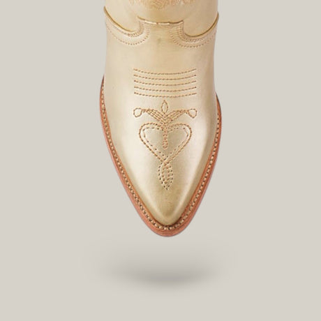 The Linda Tall Shaft Gold - J Toe boot from the Platinum Collection features a golden finish with decorative stitching and a heart-shaped pattern. Its pointed toe and leather sole are highlighted against a plain light gray background.