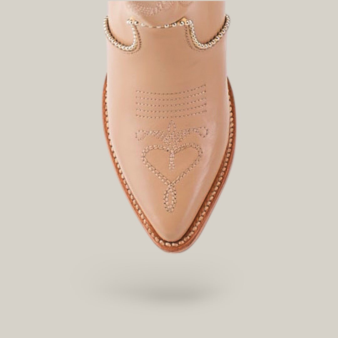 A close-up shows the intricate heart stitching and line details on a tan boot from the Platinum Collection. It features a pointed toe with metal chains around the top edge, similar to the Linda Studs Tall Shaft Cream - J Toe style, against a plain background.