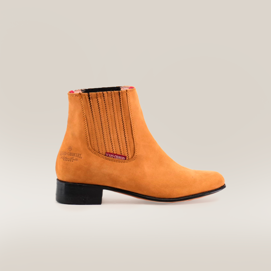 The Prime Suede Honey Round Toe ankle boot in tan leather boasts an elastic side panel, low black heel, stitched accents, a round toe, the brand embossed near the heel, and a plaid lining. Ideal for enhancing a Cowboy Scene. Presented on a white background.