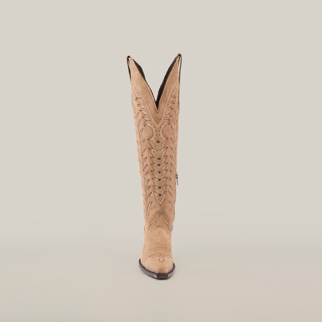 A single Madona Sand Suede boot is displayed upright on a white background. The tall shaft features intricate stitching, a snip toe, and a distinctive V-shaped top, all crafted from fine light tan suede.