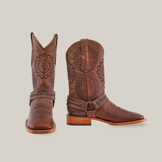 A pair of Matte Brown Country Stitch - Square Toe boots features premium cowhide with intricate embossed floral designs. Displayed upright and sidelong, the detailed patterns and wooden heels stand out against a plain white background.