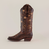 Discover the Dariela Brown Mid Shaft boot, a single cowboy boot featuring exquisite floral embroidery with swirls on a plain white background. Its medium-height heel enhances the handcrafted leathers rich texture and showcases artisanal excellence.