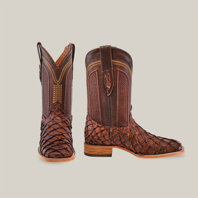 A pair of Exotic Piraruco Fish - Matte Brown - Square Toe cowboy boots, featuring a textured scaly lower reminiscent of Piraruco boots and smooth leather uppers, is showcased against a plain white background.