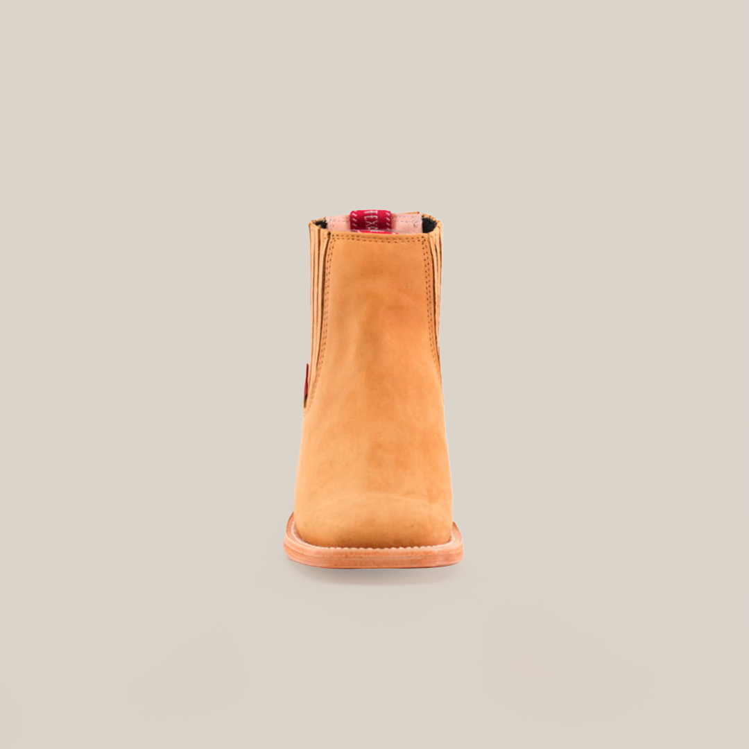 The Prime Suede Honey Square Toe is showcased against a white background. Featuring a tan suede hue, this ankle boot has a flat sole and square toe. A red plaid and beige pull tab adds contrast, embodying the Cowboy Fashion trend.