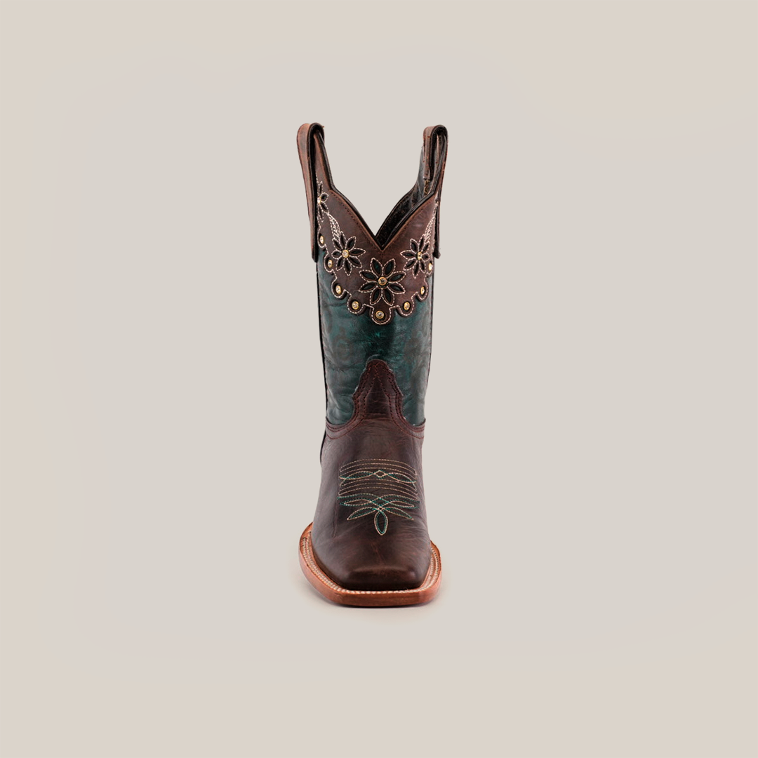 The Grecas Brown boot combines traditional craftsmanship with brown leather and turquoise accents. Its short shaft displays floral embroidery in gold and green thread. This luxurious western footwear features a square toe and wooden heel, all set against a white backdrop.