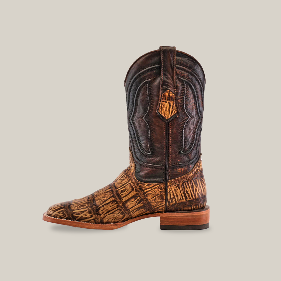 The Gator Print Orix - Square Toe is a handcrafted cowboy boot, showcasing a textured, dark brown cowhide leather upper with intricate stitching and a lighter Gator Print Orix design on the foot and lower shaft, completed by a wooden heel against a plain white background.