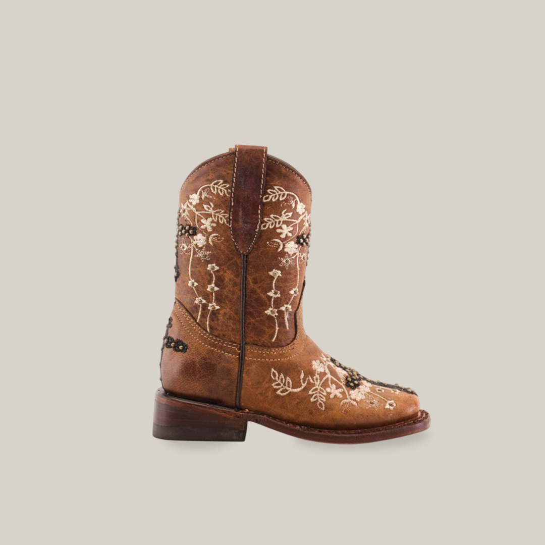 The Margacruz Studs Orix - Square Toe, a brown cowboy boot, is handcrafted from premium leather with delicate white floral embroidery on the side. Displayed against a plain white background, it highlights its low heel and sturdy leather sole.