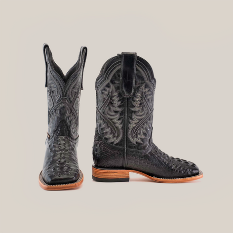 The Caiman Hornback Print Black Square Toe boots boast intricate stitching, a striking caiman hornback print on black leather, and a light brown leather sole. The premium materials are showcased with both side and front views against a plain white background.