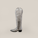 Profile view of the Brittany Silver-Tall Shaft-Snip Toe, a handcrafted metallic masterpiece with floral and leaf embroidery, pointed toe, side zipper, and low heel. Made from premium leather against a neutral gradient backdrop.