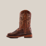 The Loggerhead Turtle Print brown Rodeo Toe boot, made from premium cowhide leather, showcases intricate stitching on the upper shaft with a textured foot design. It features a slightly raised heel and pull strap, standing upright against a plain white background.