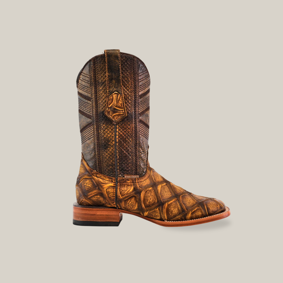 The Big Bass Pirarucu Print Rustic Honey boots feature a square toe, intricate patterns, and textures on premium cowhide. Handcrafted to exude rustic sophistication, they are set against a plain white background showcasing their unique design.