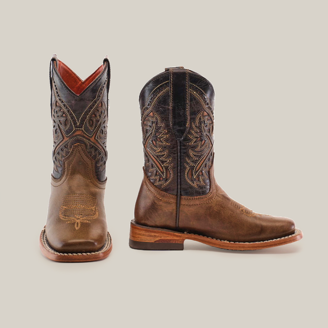 The Ranch Camel Square Toe cowboy boots, crafted from brown cowhide leather, feature intricate stitching and a decorative shaft pattern. With square toes and stacked heels, they exude western elegance. One boot faces forward while the other is side-facing.