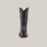 The Exotic Ostrich - Black - Rodeo Toe boot is a single black cowboy boot made of genuine ostrich leather, featuring a pointed toe and intricate stitching on the shaft. This handcrafted boot has a brown sole and stands upright against a plain, light background.