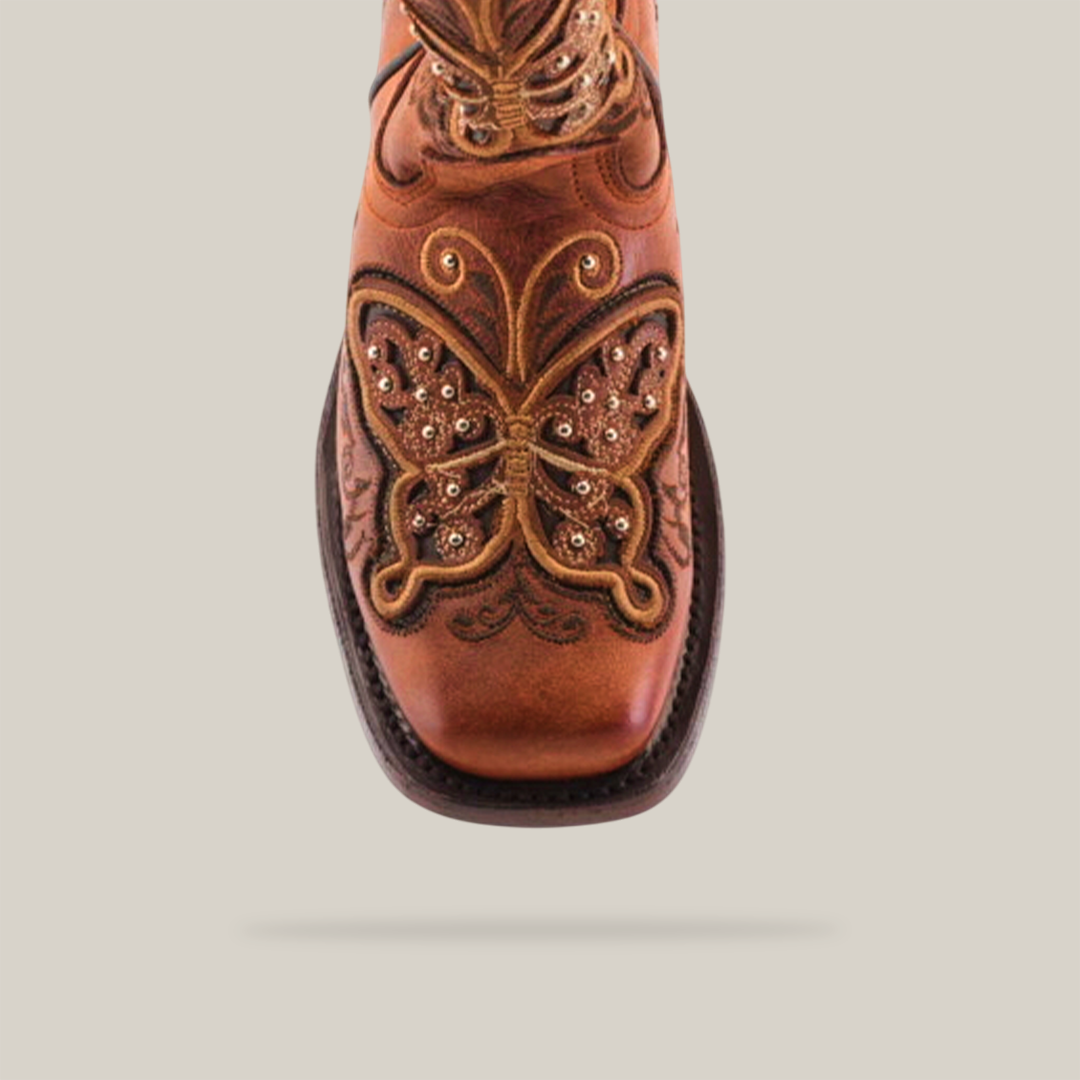 A top view of the Butterfly Studs Cogñac boot, featuring square toes and intricate butterfly embroidery on brown cowhide leather, displayed on a plain white background.