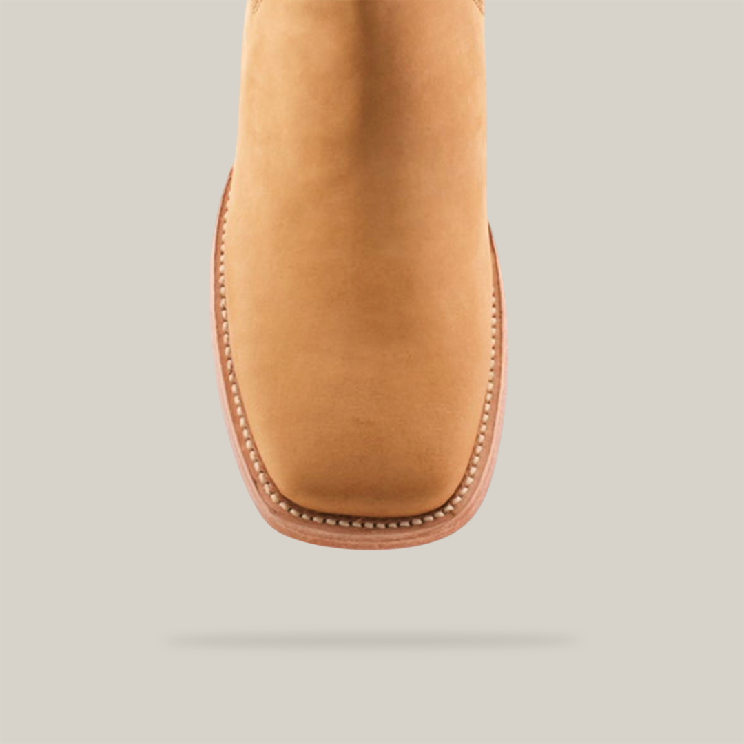 Close-up of the Prime Suede Honey Square Toe boot, featuring a tan leather finish with a rounded square toe. Detailed white stitching along the sole edge adds cowboy flair against a light background.