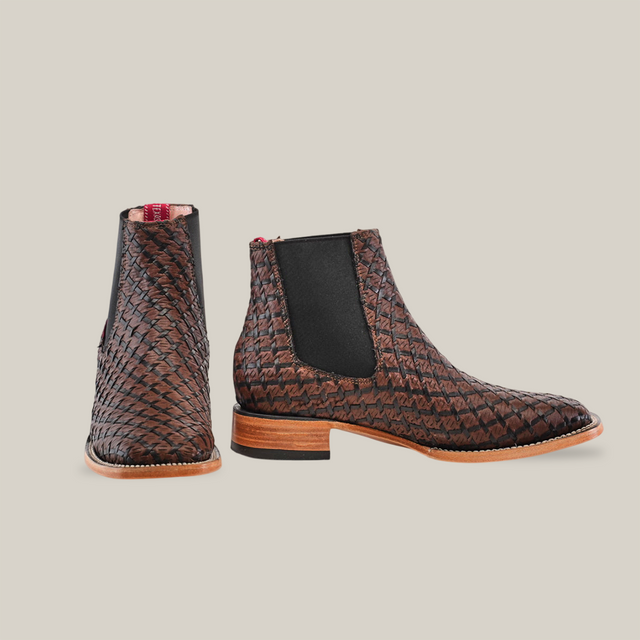 The Basket Weave BlackBrown Square Toe ankle boots feature a basket weave design, black elastic side panels, and a reddish-brown wooden heel. The left boot is shown facing forward; the right in profile view, all against a plain white background, evoking classic cowboy fashion.