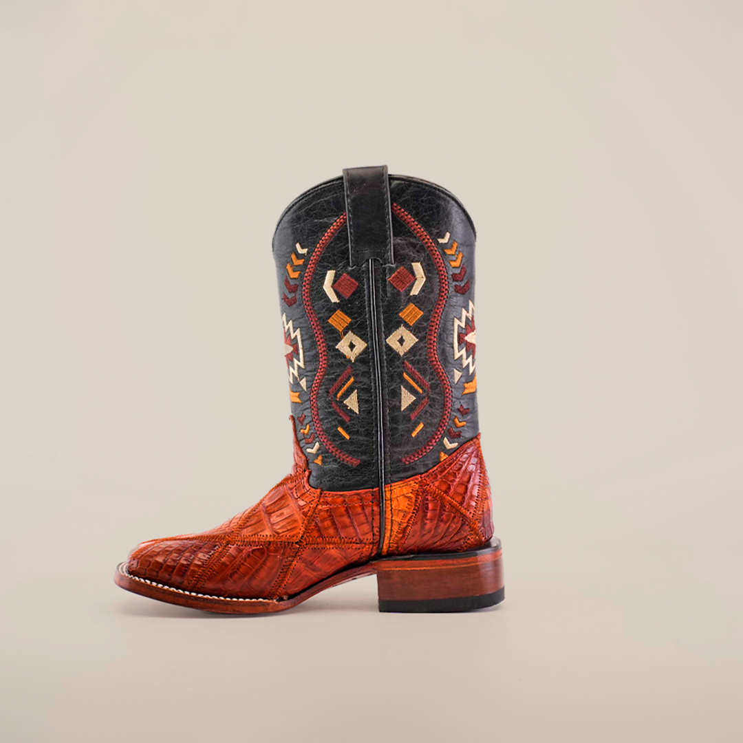 The Exotic American Alligator Patchwork Cogñac Square Toe is a single cowboy boot with Aztec-style designs and a colorful mix of brown, black, red, and orange. Its geometric patterns on the shaft pair perfectly with the smooth toe and wooden heel for a unique look.