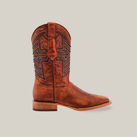 The Rustic Cogñac - Square Toe boot, made from premium cowhide leather, showcases detailed stitching, a leather pull tab, a patterned shaft with dark accents, and a low stacked heel. Seen in profile view, it embodies rustic charm with its elegant cognac tones.