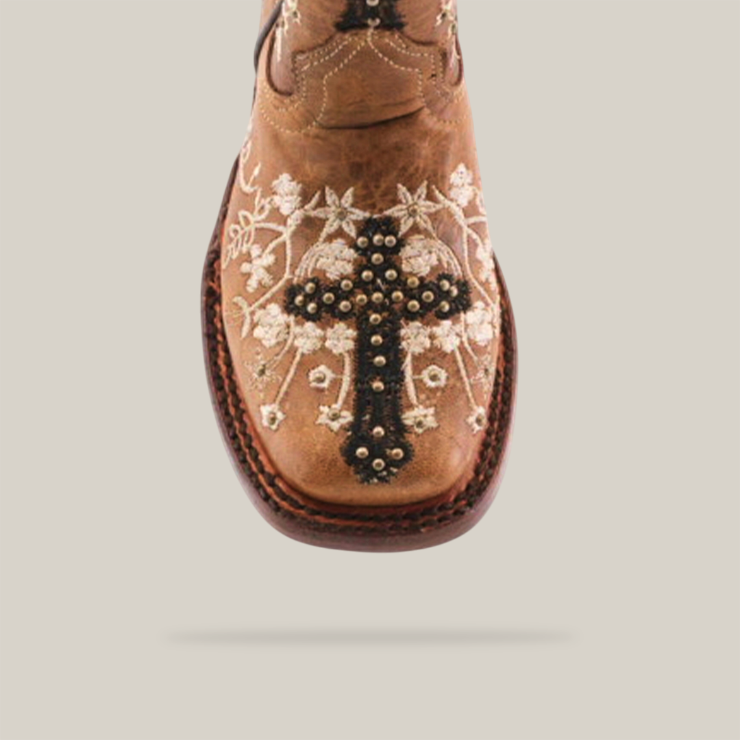 The Margacruz Studs Orix - Square Toe is a brown girls boot made from premium leather, adorned with a decorative cross and floral embroidery featuring white flowers and intricate stitching for a detailed, elegant look.