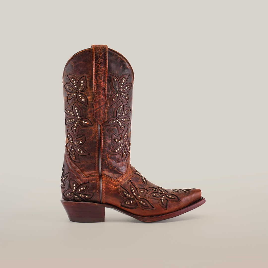 The Cosala Moka handcrafted womens cowboy boot features premium leather with intricate floral embossing and stud detailing on the shaft and foot. It showcases a snip toe and block heel, set against a plain, light background.