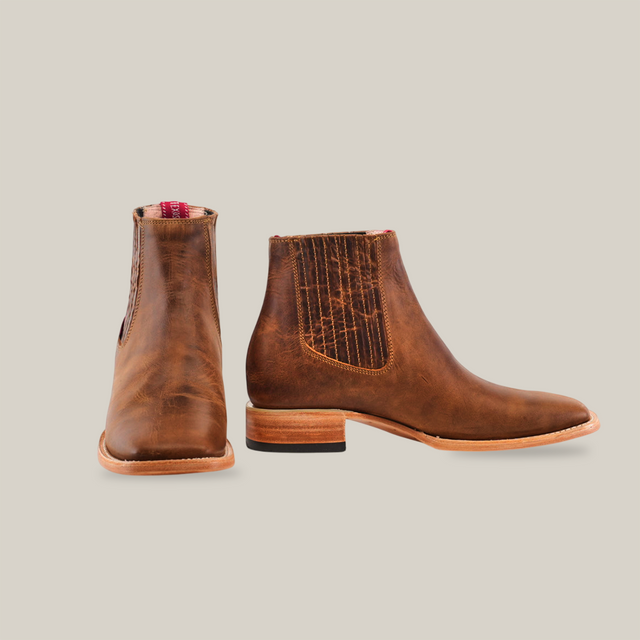 The Avejentado Honey Square Toe boot blends elegance and ruggedness, displayed on a white background. One boot stands to show its textured panel, while the other faces forward, emphasizing its cowboy-style light wooden sole.