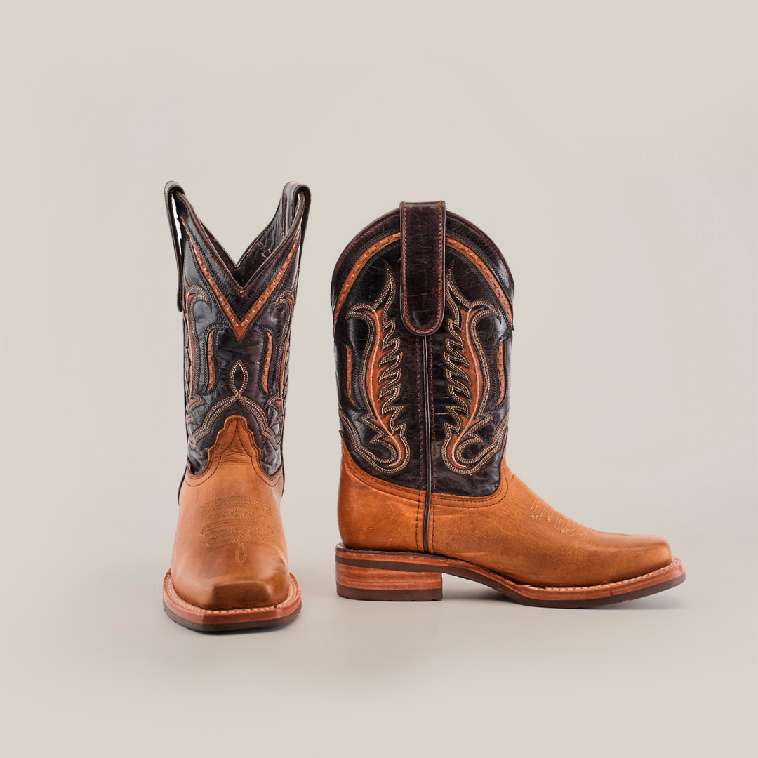 The Cater Honey Slip Resistant Sole Rodeo Toe boots showcase ornate dark leather detailing on the premium brown leather shafts. The featured rodeo toe design stands upright against a plain white background, capturing both side and front views.