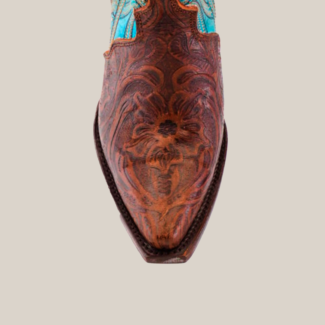 A close-up of the Premier Tabaco Handtooled Flowers boot reveals intricate brown leather floral tooling and stitching on the snip toe, contrasted by a blue leather tall shaft, highlighting its Western elegance