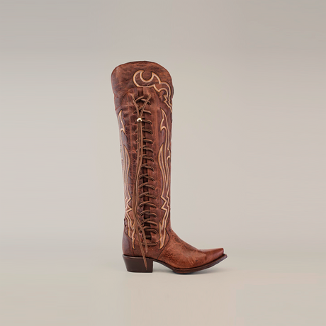 The Tania Brown boot features a tall shaft with intricate embroidery and side lacing, crafted from luxurious brown leather. It boasts a snip toe and short block heel, presented against a plain white background.