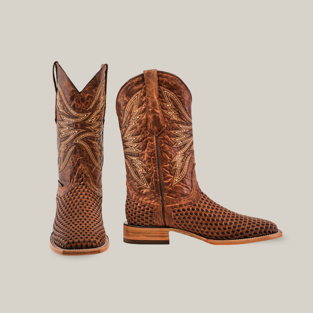 The Texas Basket Weave Orix boots are crafted from premium brown cowhide leather, featuring intricate stitching and a textured design. The left boot stands upright, while the right lies on its side, revealing the wooden sole and heel. Both square-toe boots come with pull tabs for easy wear.